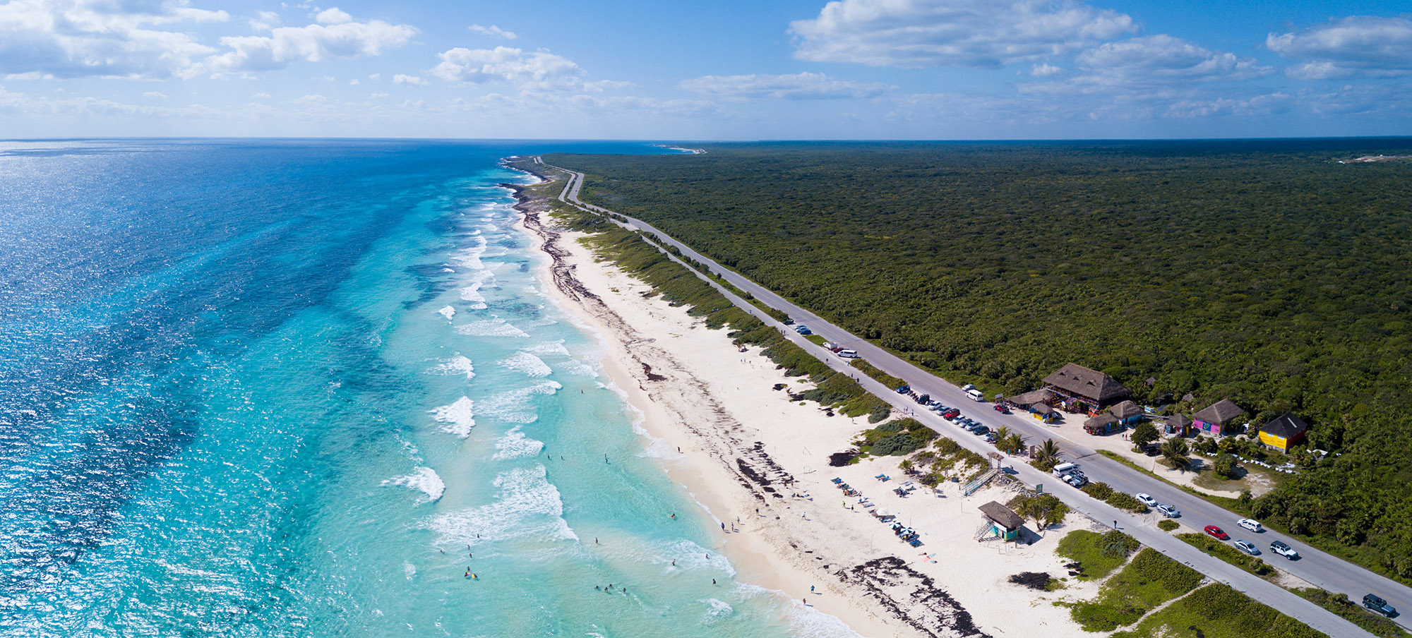Aerial view of a long stretch of white sand beach with small turquoise waves crashing on the beach 