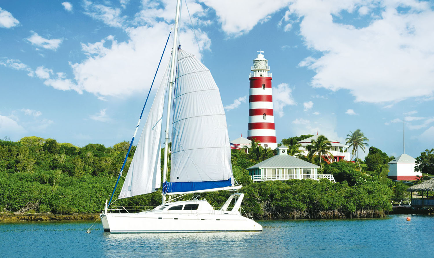 Yacht sailing past tropical island with red and white striped lighthouse