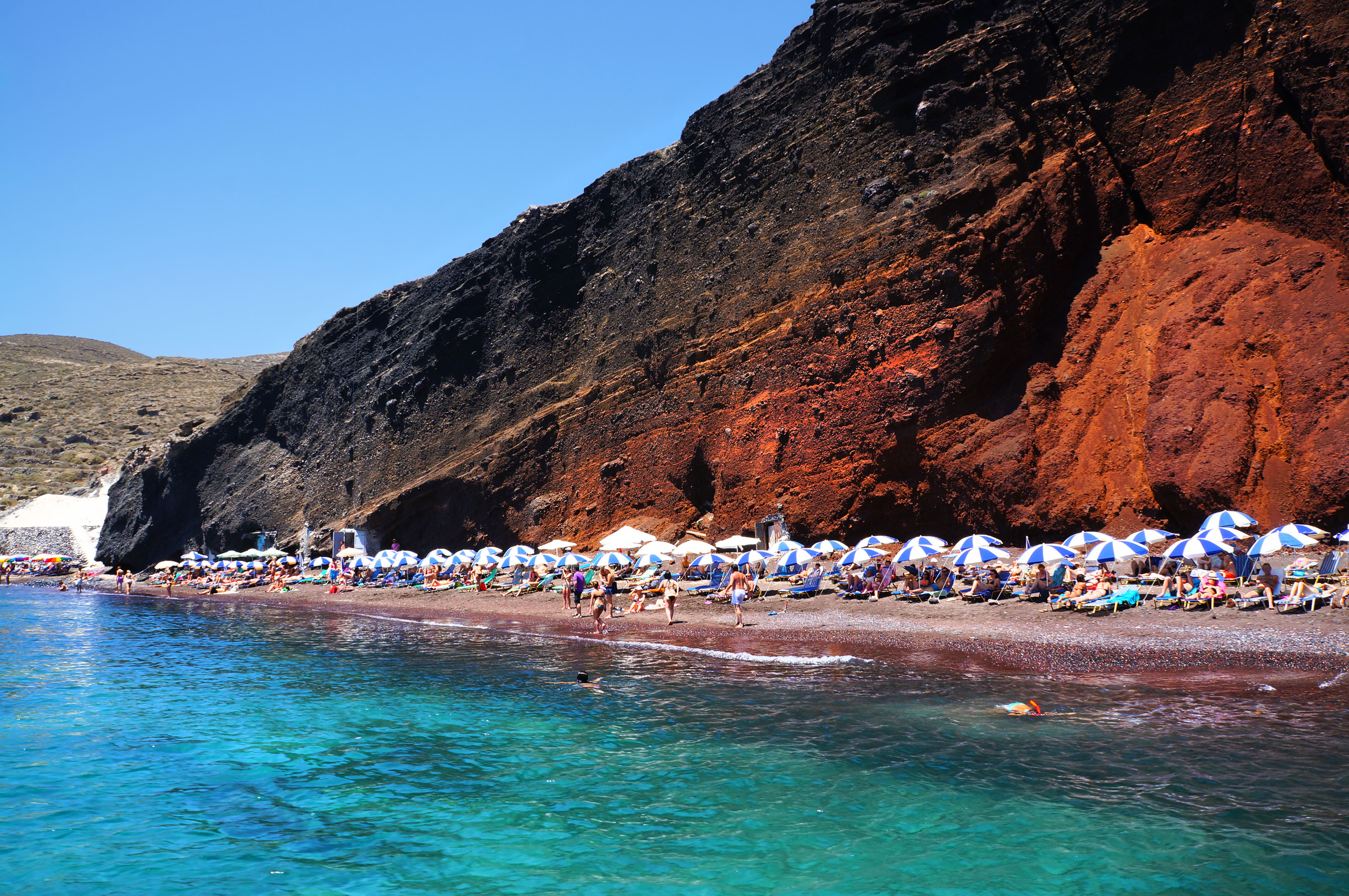 beachgoers sunbathing on Red Beach in Santorini by turquoise sea and red cliffs