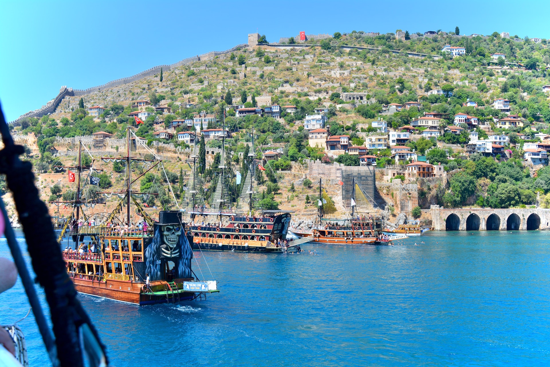 view of Antalya from the sea with blue ocean reflecting ancient stone architecture and green hills behind