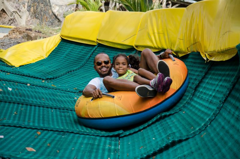 Man and young girl sitting in yellow tube sliding down green track