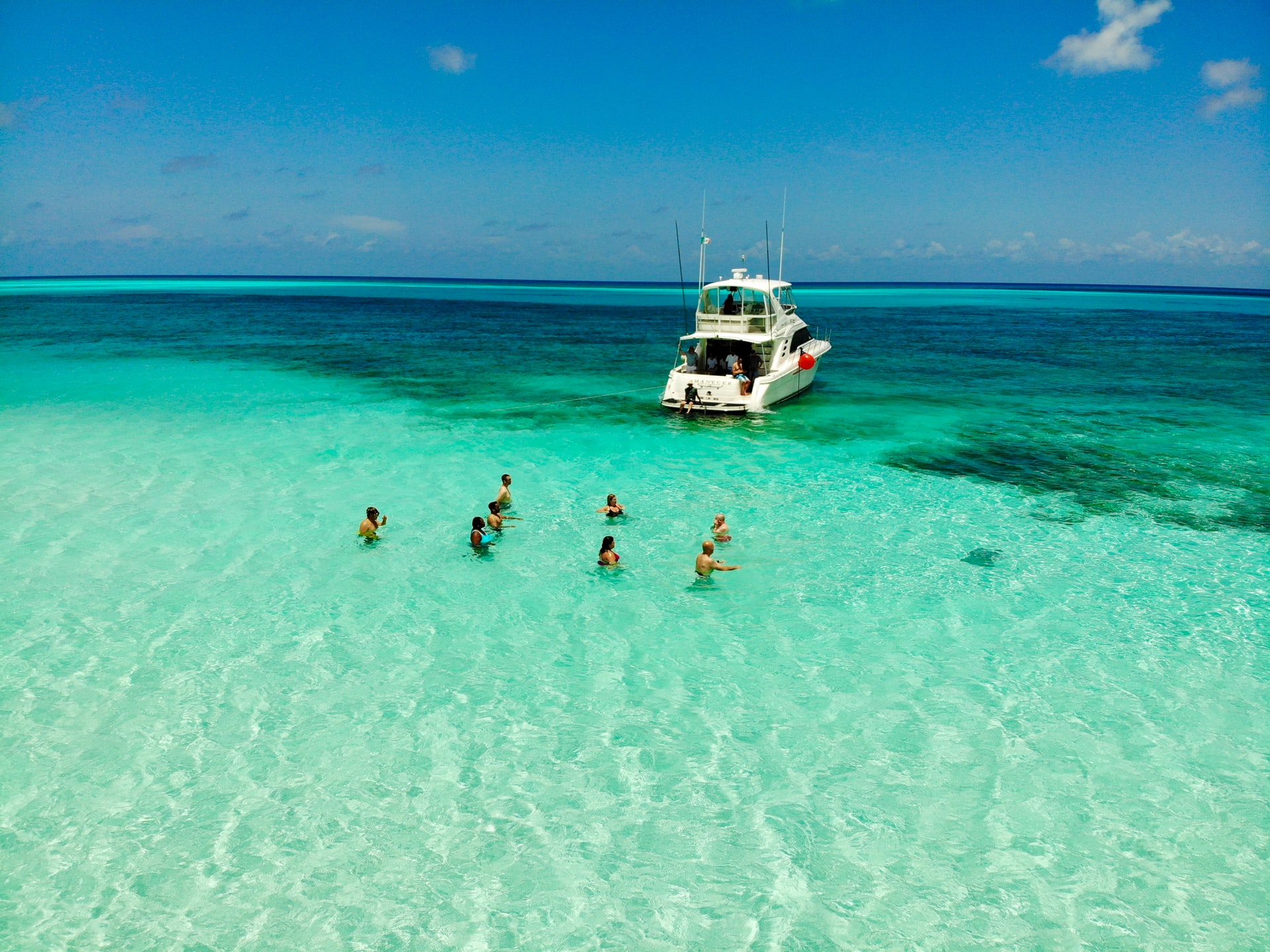 People in clear green sea in the Caribbean next to docked yacht 