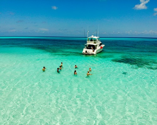 People in clear green sea in the Caribbean next to docked yacht