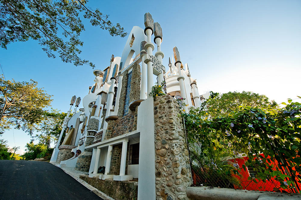 A white and stone building on a street surrounded by trees