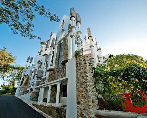 A white and stone building on a street surrounded by trees