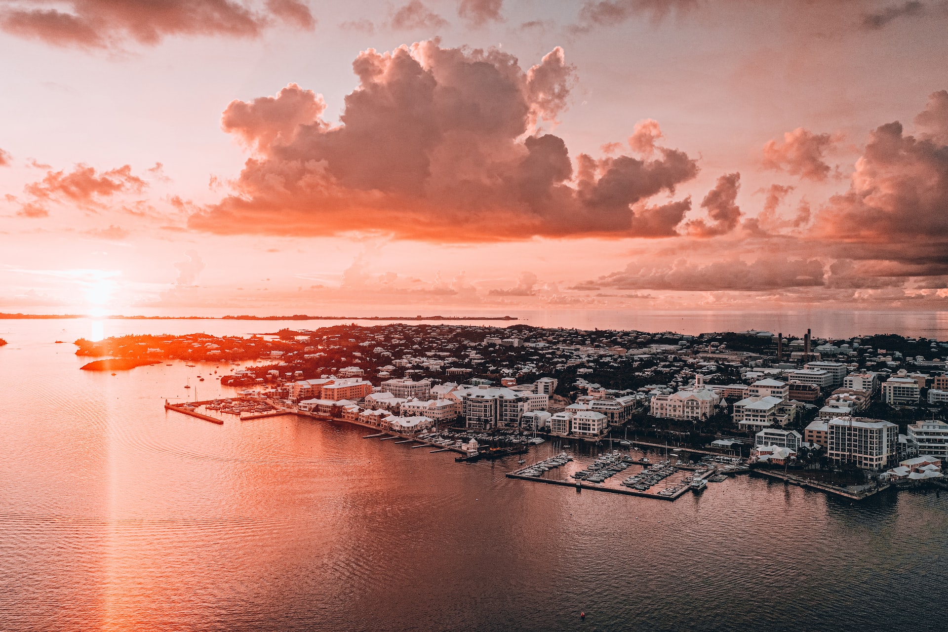 Aerial view of a red sun set in the distance above a town on the edge of an island