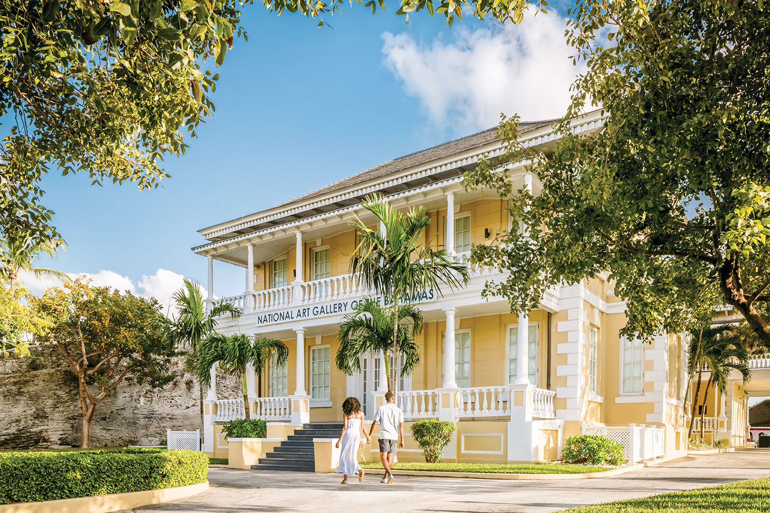 Couple walking past large yellow building in tropical setting