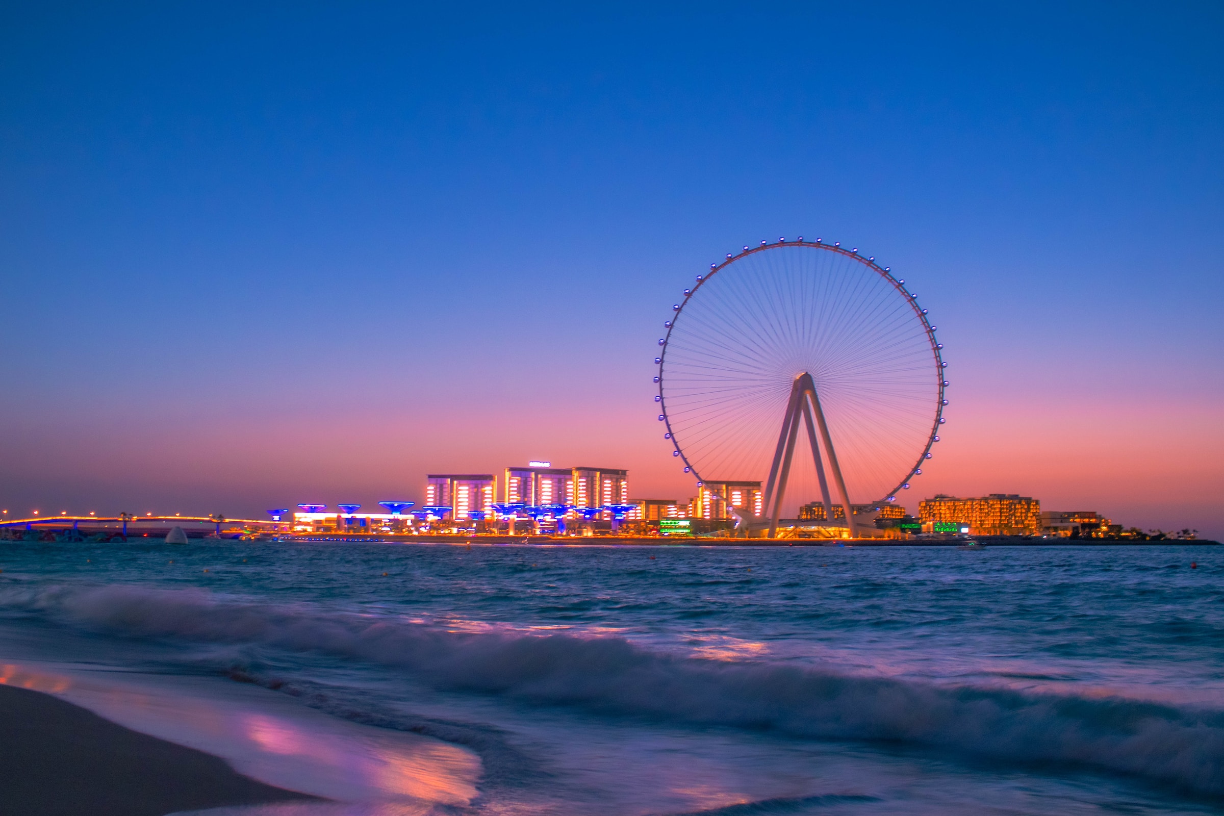A ferris wheel at sunset opposite a beach