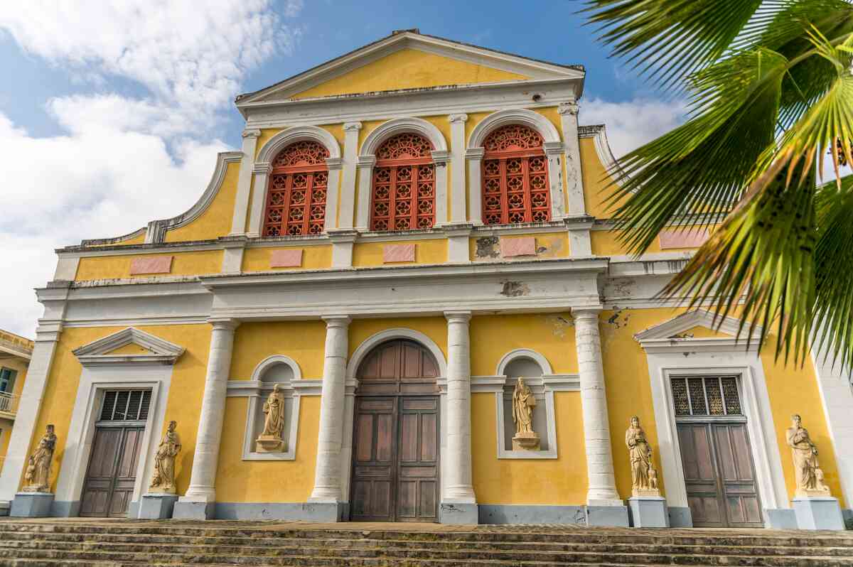 Exterior of yellow church building with religious statues by the doors