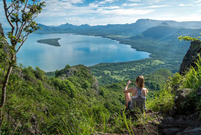 A woman sitting at the top of a hill admiring the view of the jungle below