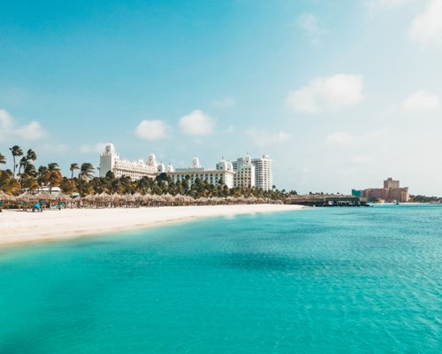 Turquoise sea and white sand with straw umbrellas for shade and hotels in the distance that surround Palm beach