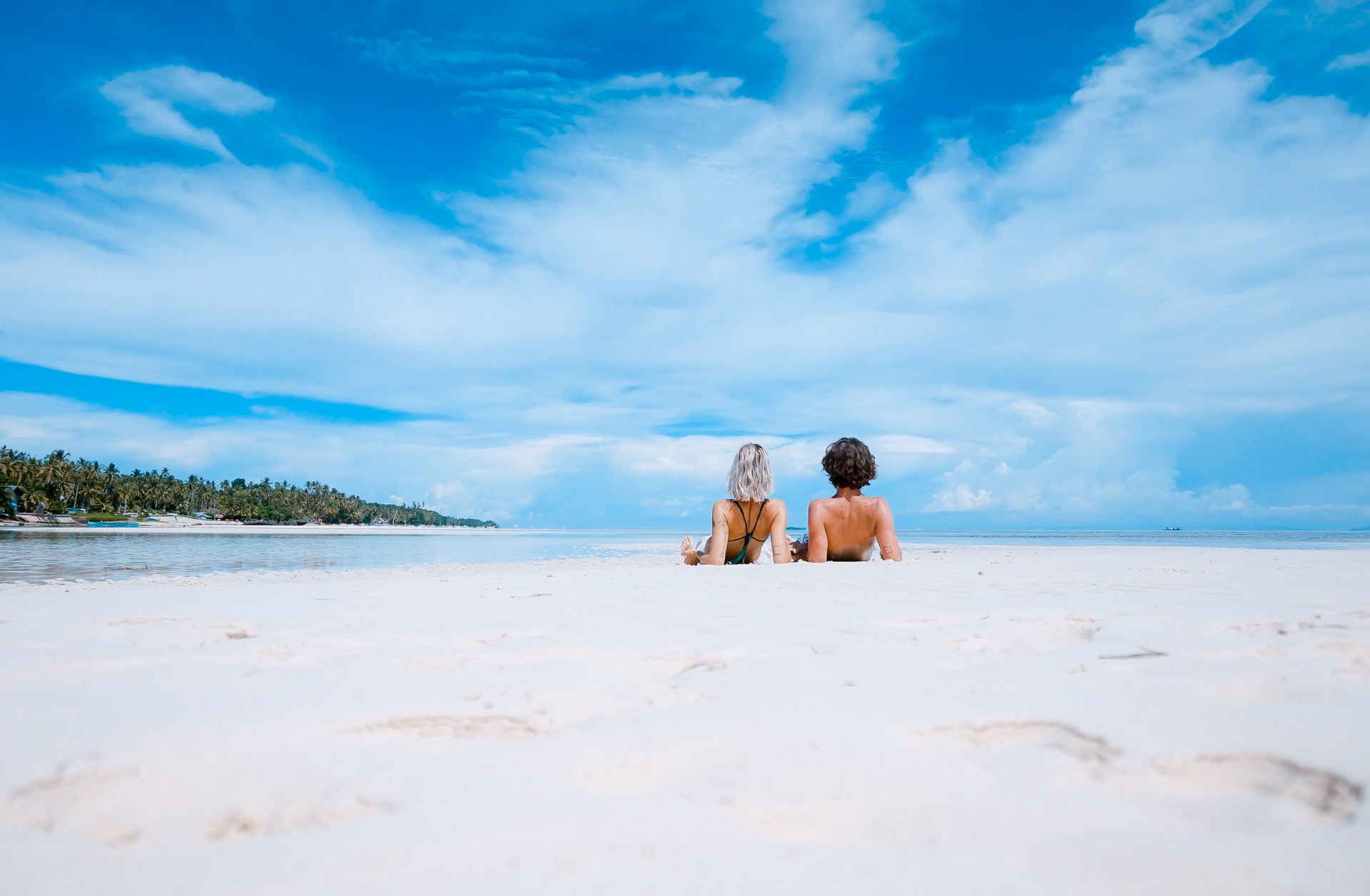 Young couple sitting on tropical beach looking out to an island in the sea