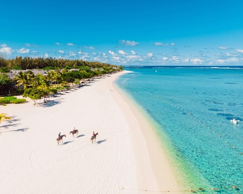 Three people riding brown horses on a tropical white sand beach in Mauritius