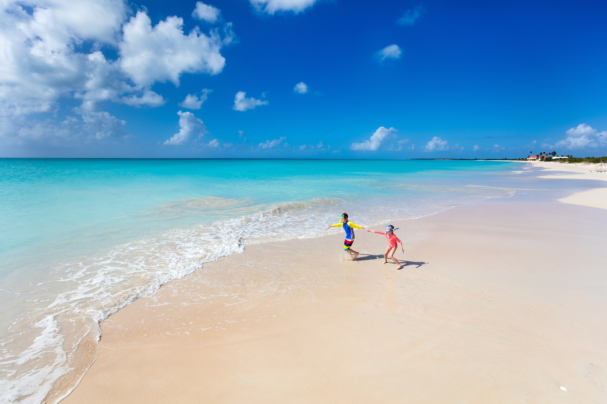 Two kids having fun at the beach running across white sand towards beautiful turquoise sea