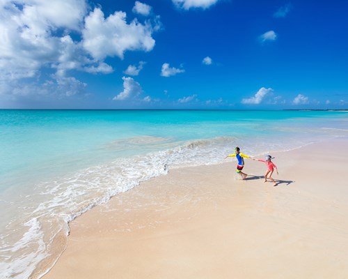 Two kids having fun at the beach running across white sand towards beautiful turquoise sea