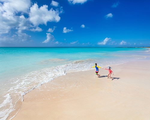 Two kids having fun at the beach running across white sand towards beautiful turquoise sea