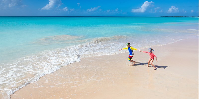Two kids having fun at the beach running across white sand towards beautiful turquoise sea