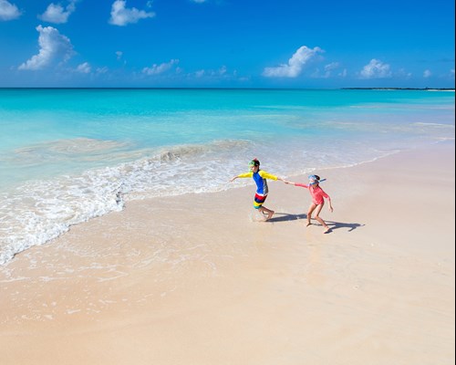 Two kids having fun at the beach running across white sand towards beautiful turquoise sea