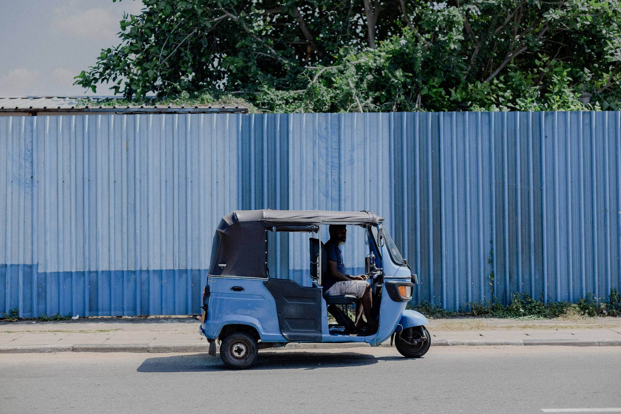 Blue tuk tuk driving alone with blue fence in background