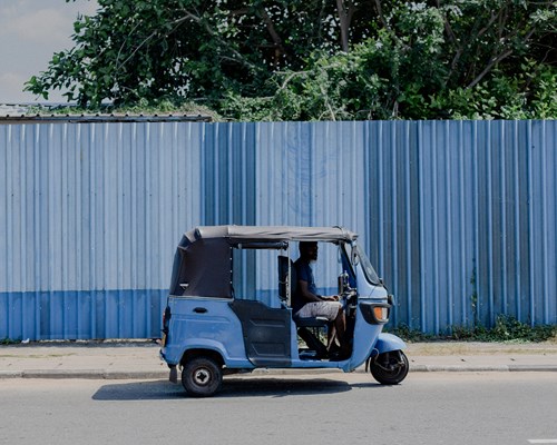 Blue tuk tuk driving alone with blue fence in background