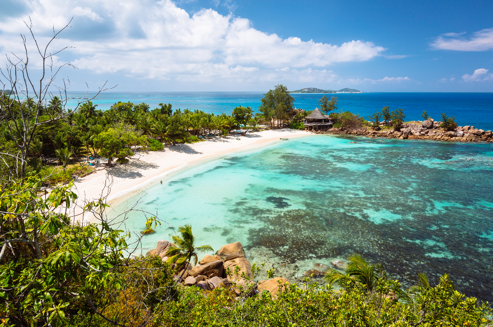 Turquoise waters edging onto to white sand with lush vegetation around the perimeter - Petite Anse Kerlan 