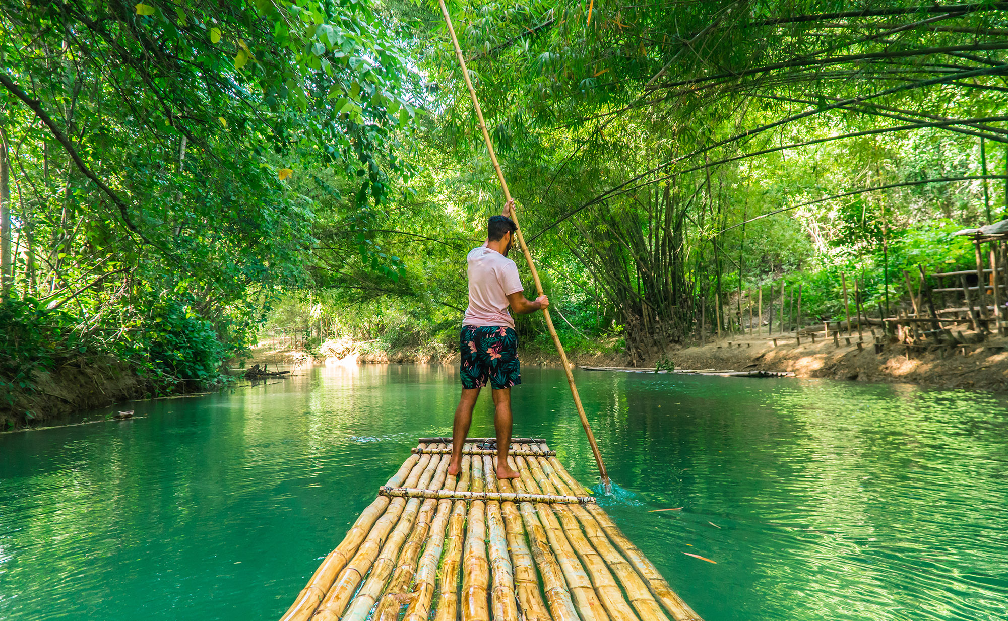 Man rowing bamboo raft along a bright green river in Jamaica
