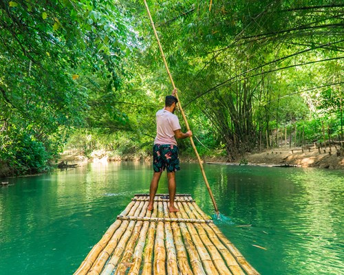 Man rowing bamboo raft along a bright green river