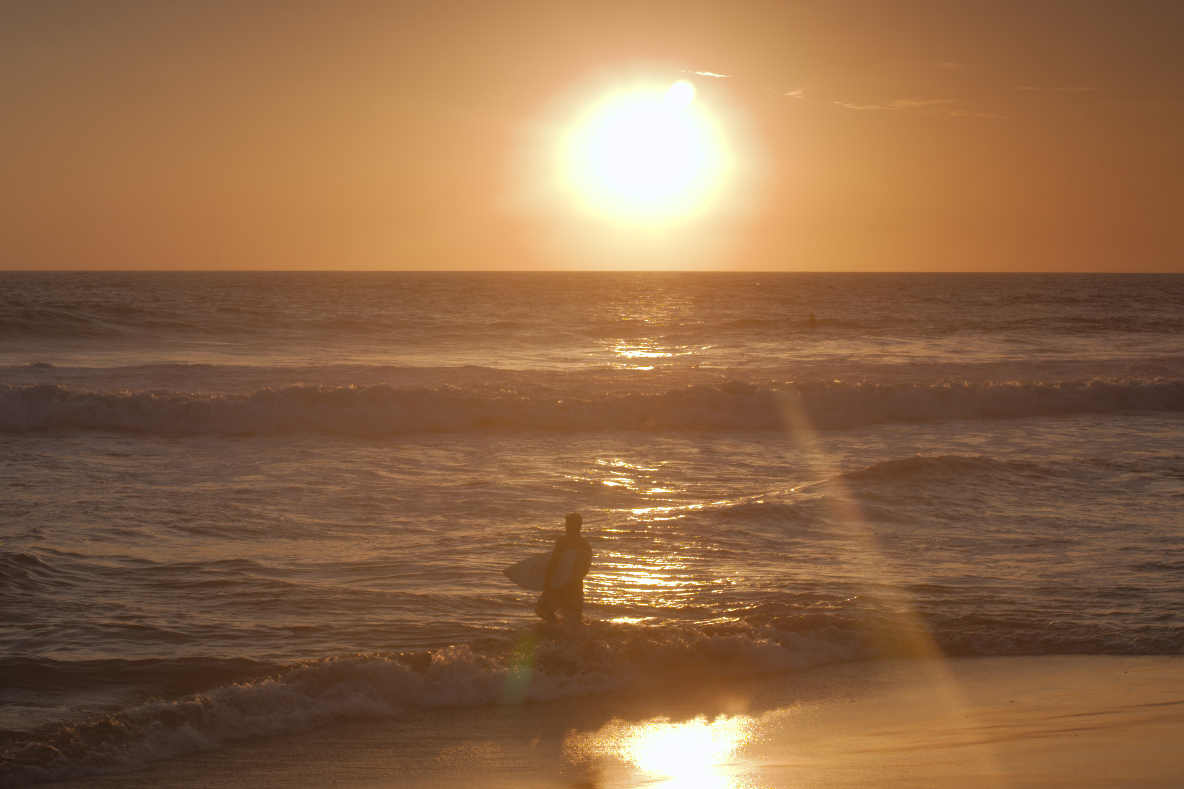 Surfer carries board through sunset on Echo Beach in Bali