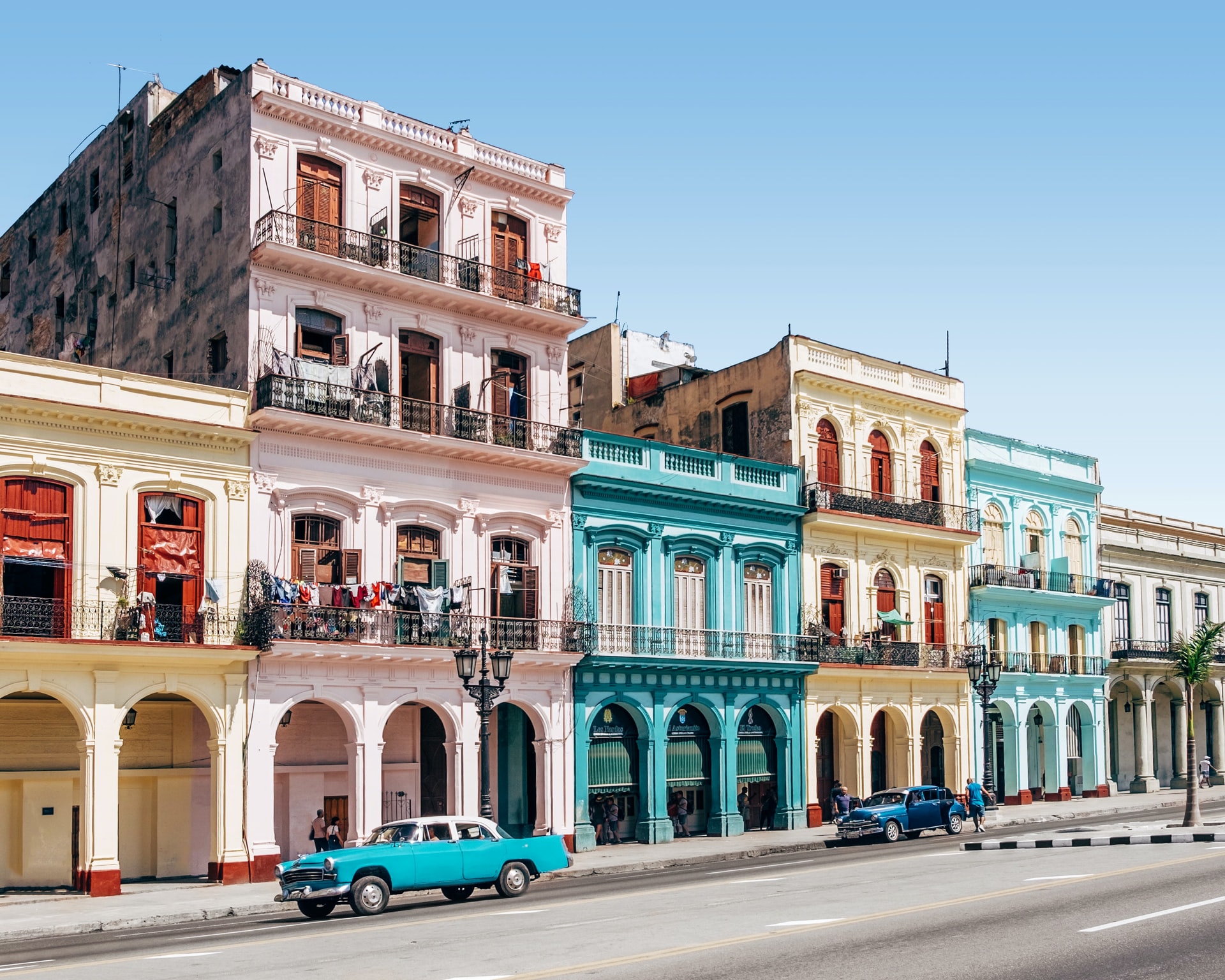Two blue cars parked outside a street of colourful buildings in a summer destination