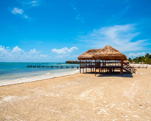 Beach hut with straw roof on an empty golden sand beach lapped by a turquoise sea