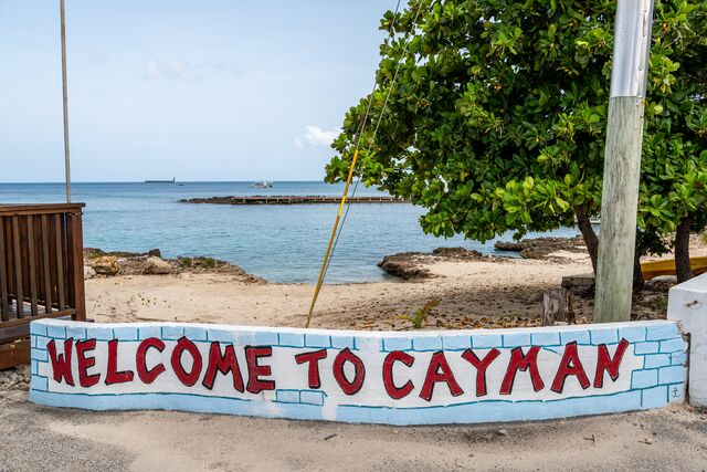 Welcome to Cayman sign with a beach and leafy trees behind it