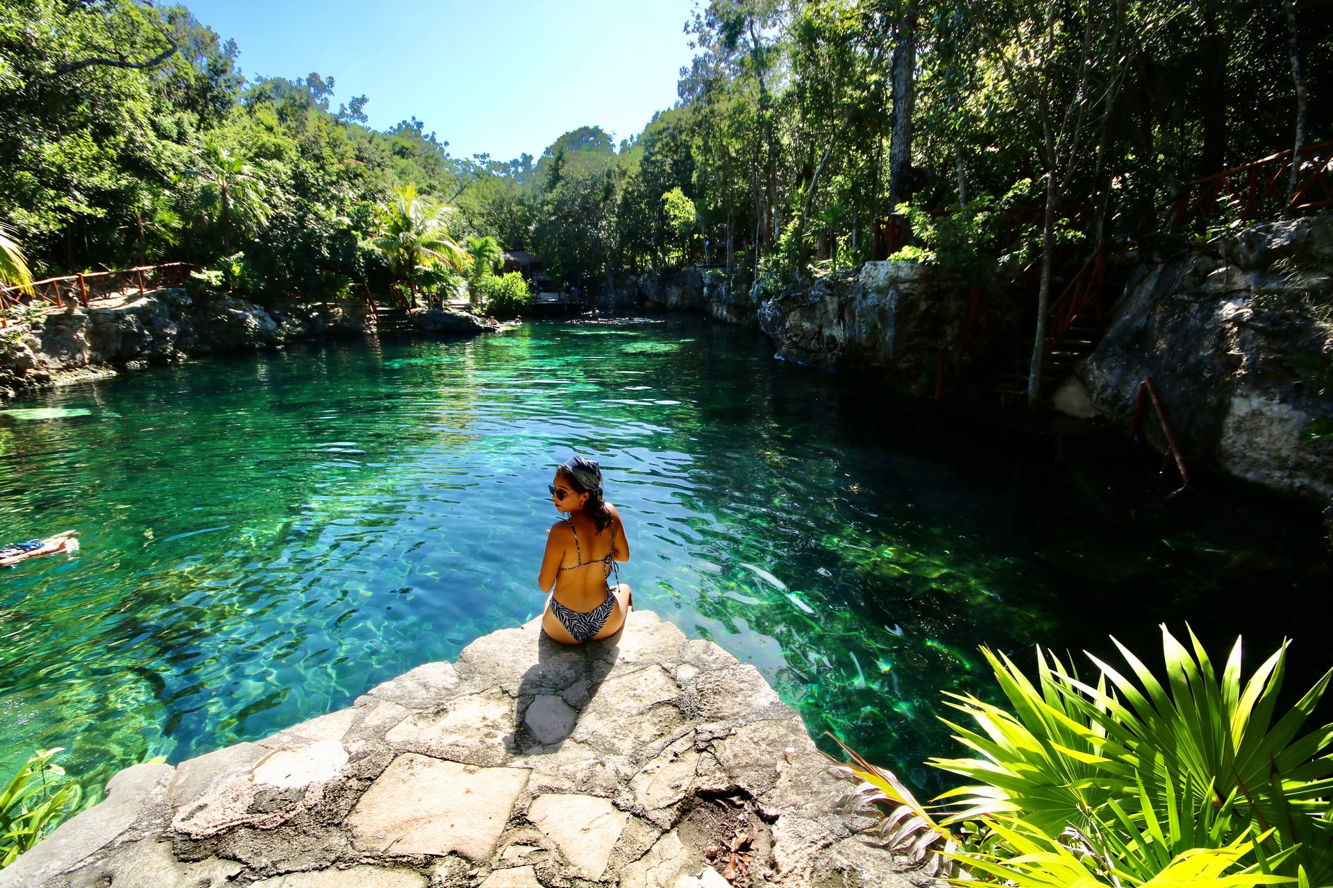 Woman wearing a bikini sitting on a rock next to a bright green pool of water -