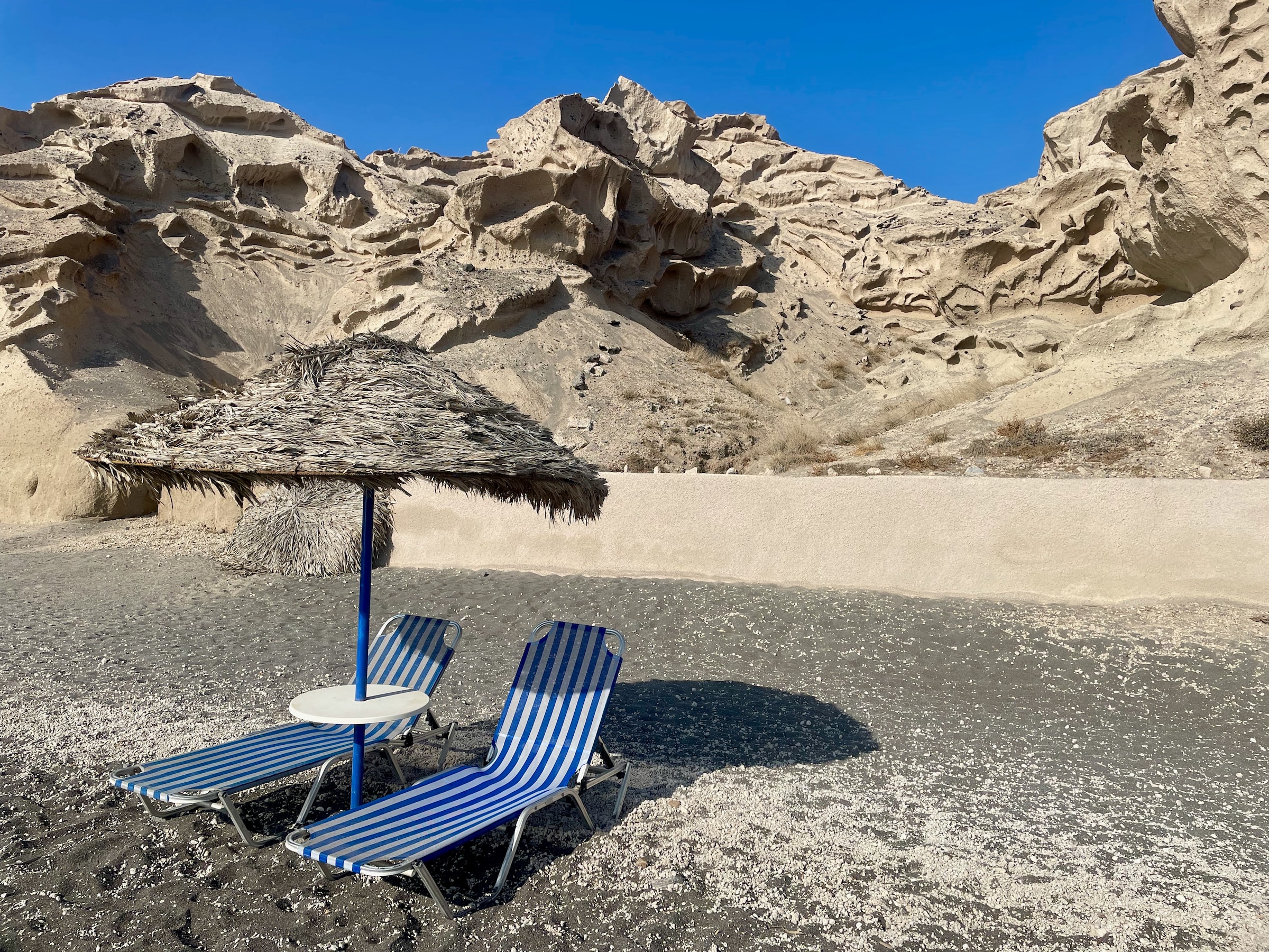 A thatched parasol and sun beds on a grey-toned beach