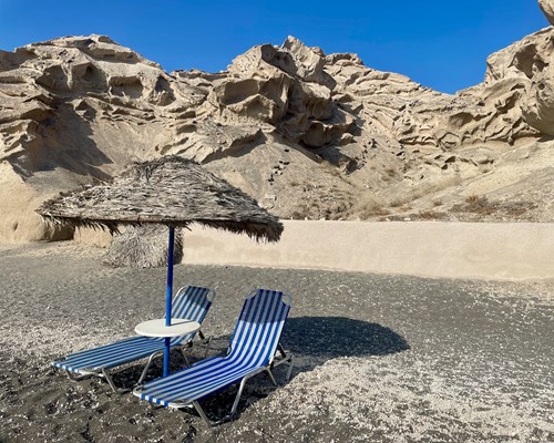 A thatched parasol and sun beds on a grey-toned beach