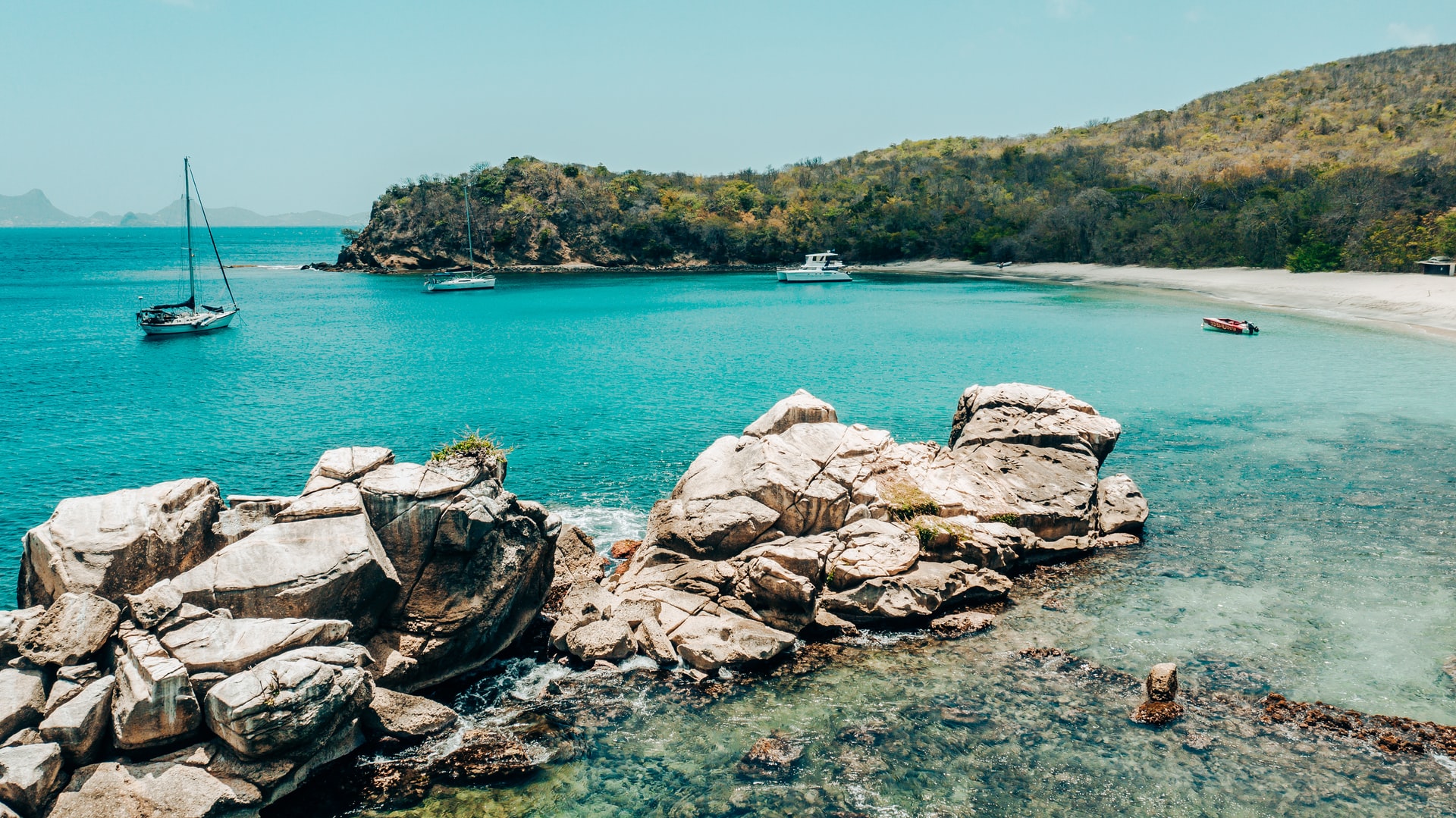 Boats docked in secluded tropical bay with bright blue sea and white sand beach