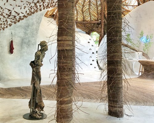 Man looking at a grey statue in a round white room with straw ceiling in an eco resort in Mexico