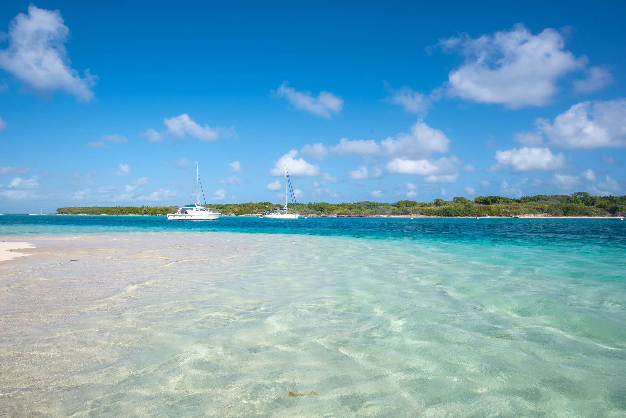 2 yachts in clear blue sea docked by tropical island