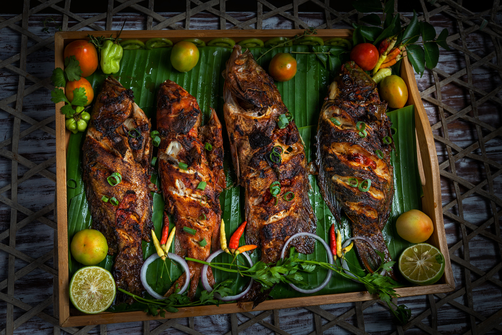 Roasted fish with colourful vegetables laying on a bed of palm leaves 