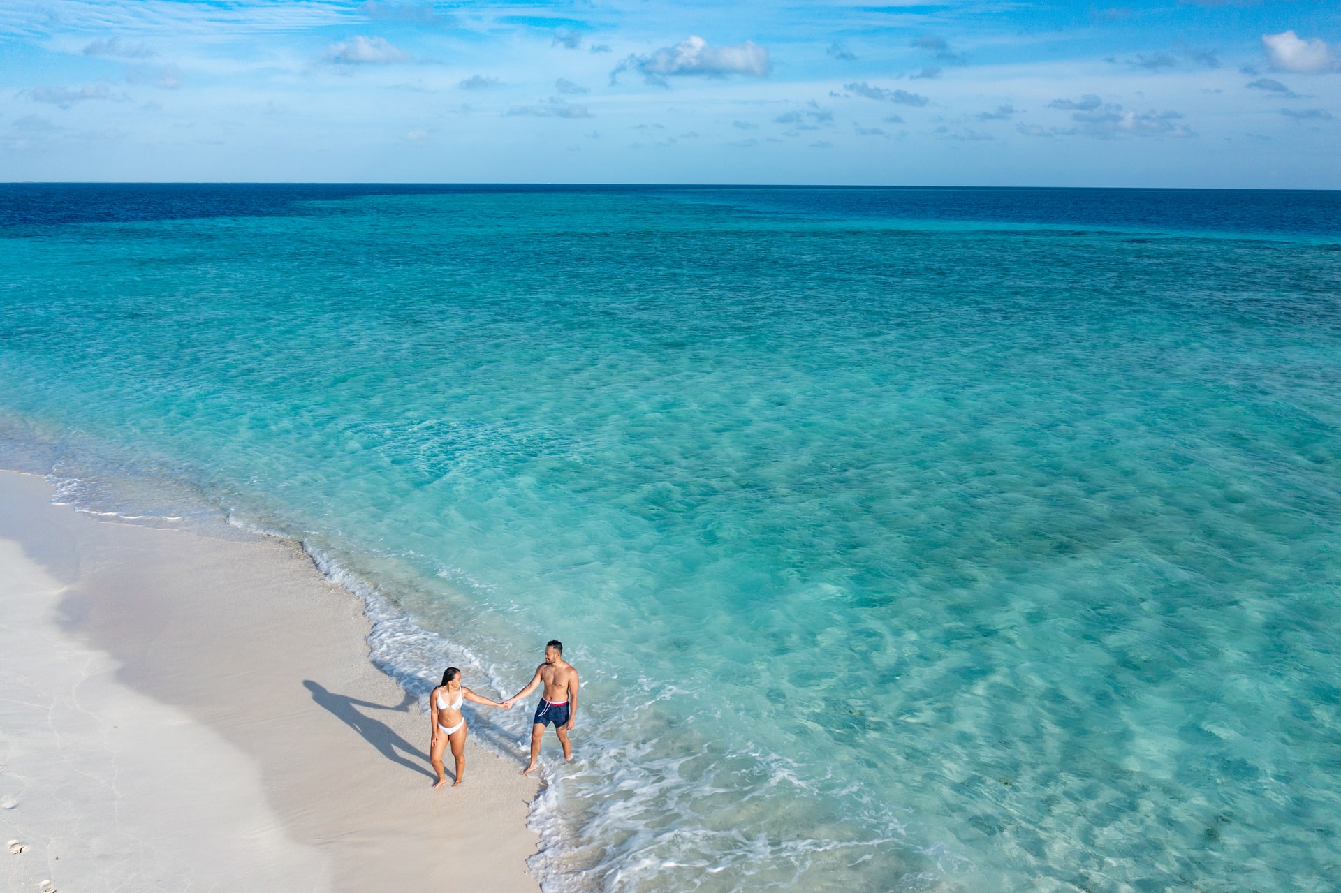 Aerial view of a man and woman in swimwear walking out of clear blue sea on to a white sand beach