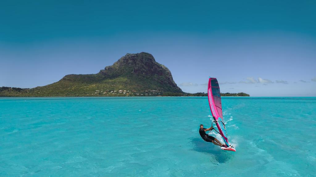 Man parasailing in the middle of turquoise sea with mountains in the background