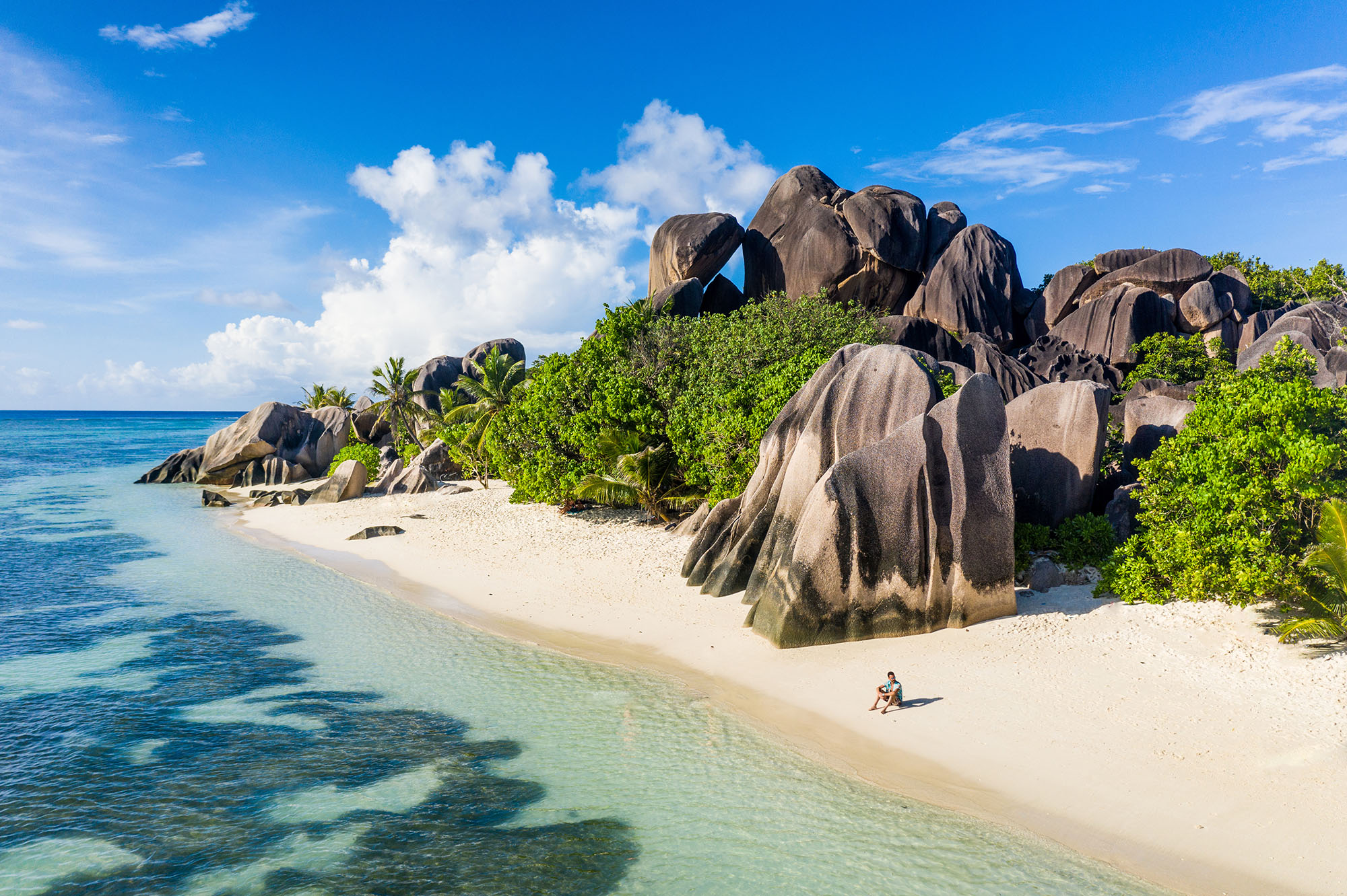 Man sitting next to large rocks on a tropical beach