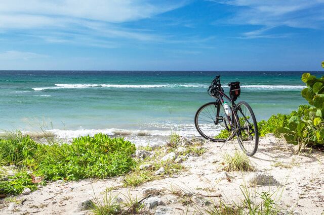 Bicycle alone on whie sand with green bushes and blue ocean in background - Cemetry Beach, Cayman islands 