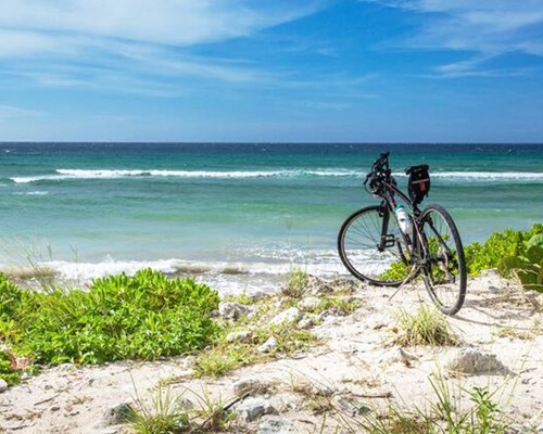 Bicycle alone on whie sand with green bushes and blue ocean in background - Cemetry Beach, Cayman islands