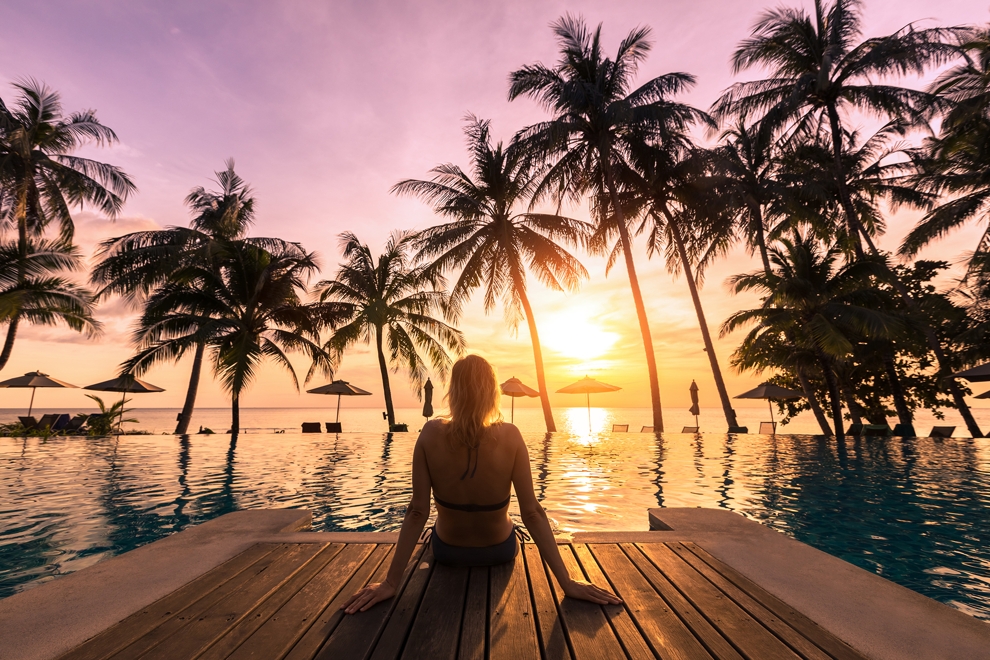 Woman relaxing by a pool in a luxury resort watching the sun set into the sea
