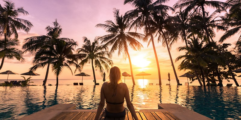 Woman relaxing by a pool in a luxury resort watching the sun set into the sea