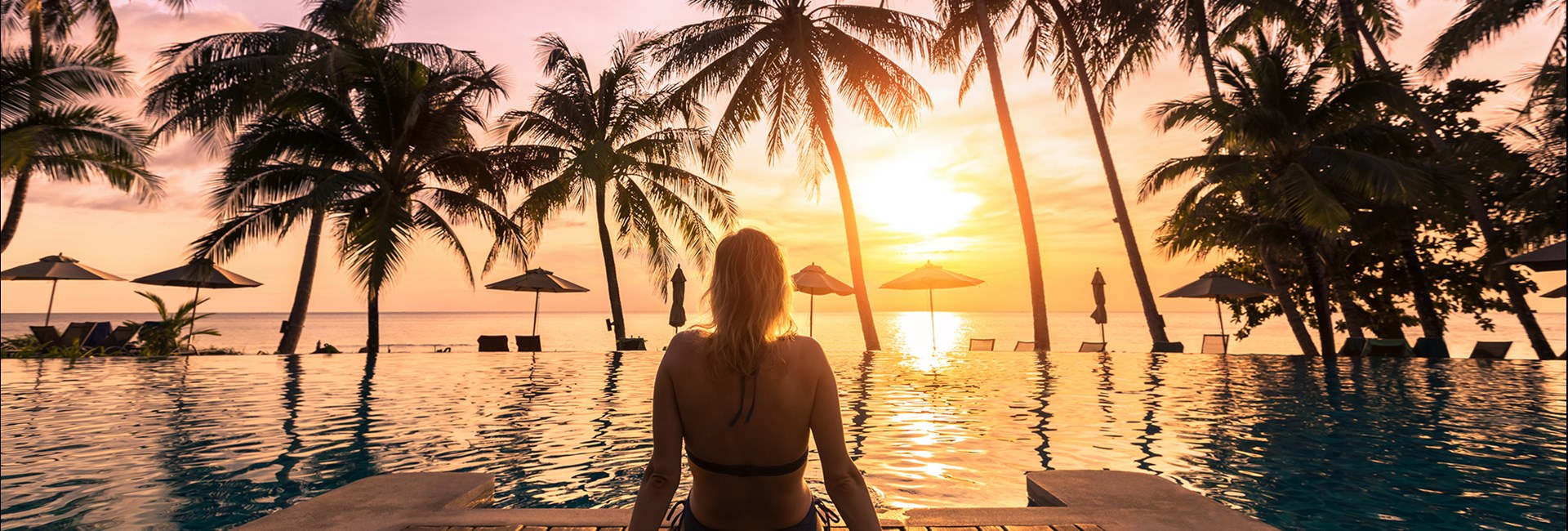 Woman relaxing by a pool in a luxury resort watching the sun set into the sea