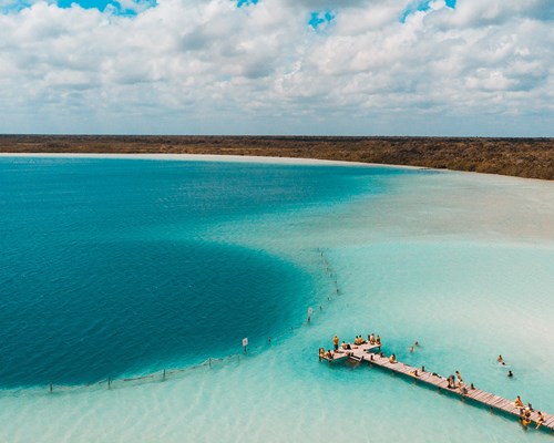 People standing on a wooden walkway over the sea leading to a large dark blue circle of water