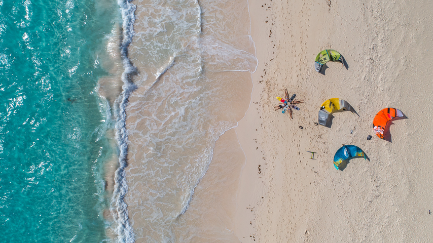 Kiteboards on sandy beach next to crystal waters