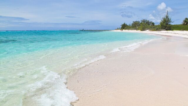 Turquoise waters crashing on white sand with trees in distance - Seven Mile Beach