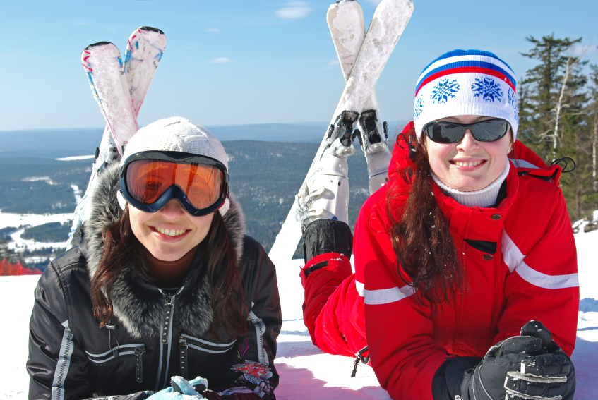 two girls in ski gear lay in snow with skis crossed